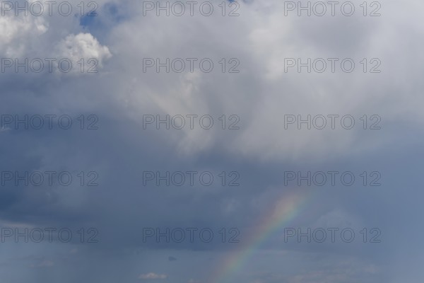 Bright sunlight breaks through large clouds after a rain shower and reveals a magnificent rainbow across the sky. The serene landscape below adds to the picturesque moment. Bas rhin, Alsace, grand est, France