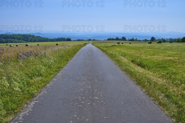 Straight road through a vast landscape of green meadows and distant hills under a blue sky, Koppelhutweg, Lange Rhön, Hausen, Rhön, Bavaria, Germany