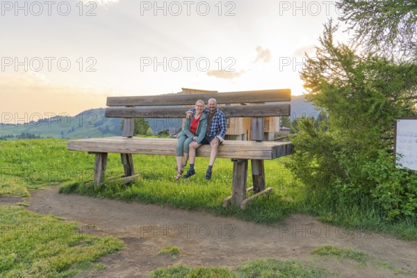 A couple sits on an oversized bench and enjoys the sunset, Alpe di Siusi, Dolomites, South Tyrol, Italy