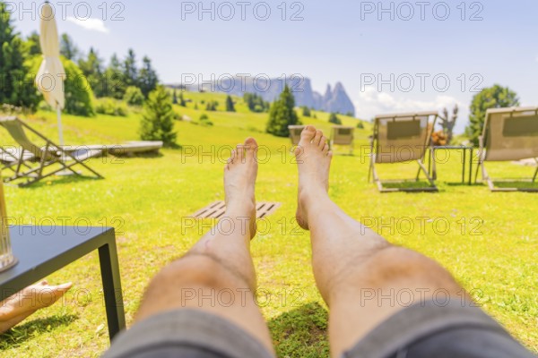 Person lying in a deckchair enjoying the summer landscape and the peace and quiet in a meadow, Alpe di Siusi, Dolomites, South Tyrol, Italy