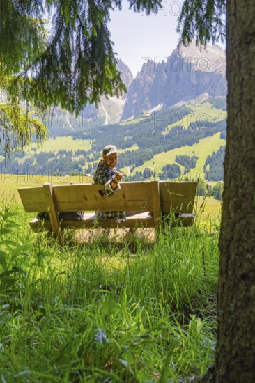 Person on a bench smiling with a peace sign in front of the mountains, Alpe di Siusi, Dolomites, South Tyrol, Italy