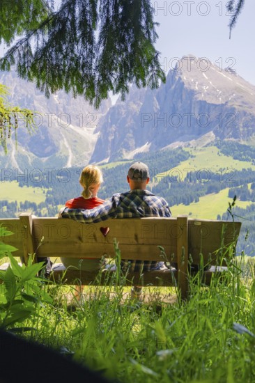Couple sitting together on a bench and looking at the mountains, Alpe di Siusi, Dolomites, South Tyrol, Italy