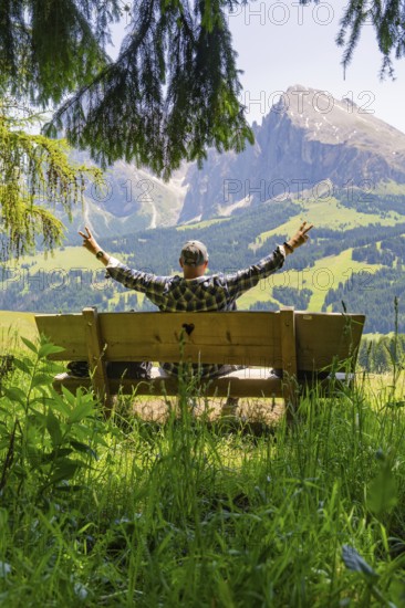 Person on a bench with outstretched arms in front of a mountain landscape, Alpe di Siusi, Dolomites, South Tyrol, Italy