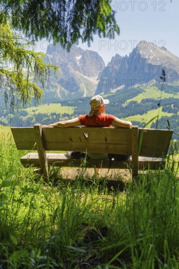 Person on a bench with a view of majestic mountains and vast landscape, Alpe di Siusi, Dolomites, South Tyrol, Italy