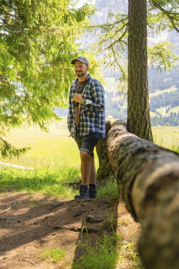 Man leaning against a tree trunk and enjoying the forest atmosphere, Alpe di Siusi, Dolomites, South Tyrol, Italy
