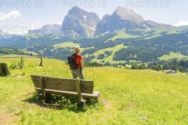 Person stands next to a bench and enjoys the view of the mountains, Alpe di Siusi, Dolomites, South Tyrol, Italy