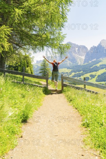 Person jumping joyfully on a path with breathtaking mountain views, Alpe di Siusi, Dolomites, South Tyrol, Italy