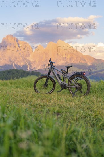 A bicycle stands in a meadow in front of an impressive mountain landscape at sunset, Alpe di Siusi, Dolomites, South Tyrol, Italy