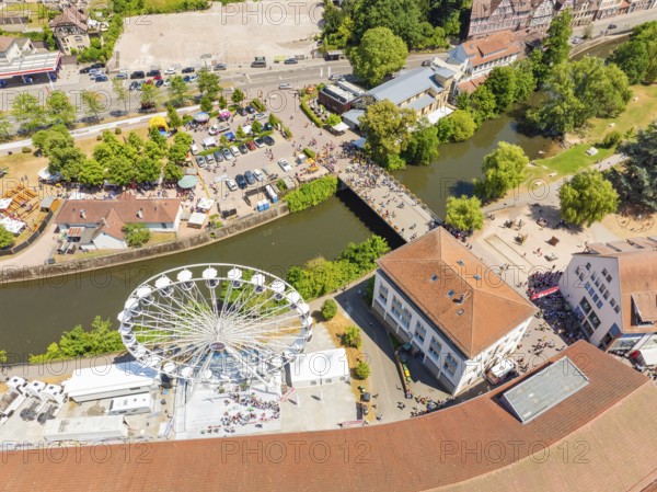 View from above of a summer festival with Ferris wheel, bridge and many people along a river in the city centre, 950 years Calw, parade Calw, Black Forest, Germany