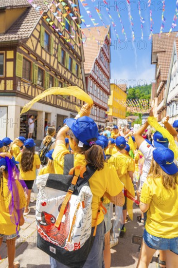 Children in yellow clothing and blue caps waving scarves in a colourful old town, 950 years of Calw, Calw parade, Black Forest, Germany