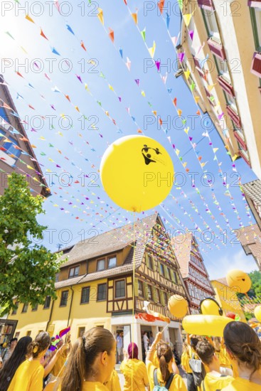 Yellow balloons rise into the sky above a busy street with historical flair and colourful pennants, 950 years of Calw, Calw parade, Black Forest, Germany