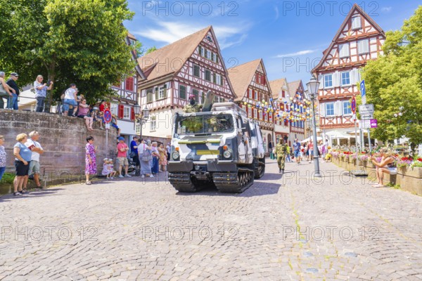 A military vehicle drives on a festive street with half-timbered buildings and people passing by, 950 years of Calw, Calw parade, Black Forest, Germany