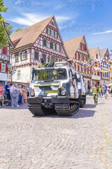A military vehicle drives past a historic half-timbered backdrop with blue sky and spectators, 950 years of Calw, Calw parade, Black Forest, Germany
