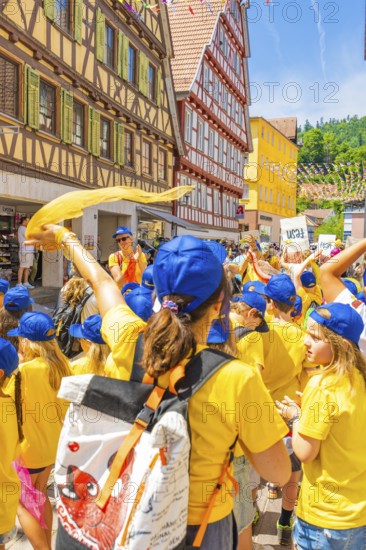 A group of children in yellow shirts and blue caps celebrates in an old town with half-timbered houses, 950 years of Calw, Calw parade, Black Forest, Germany
