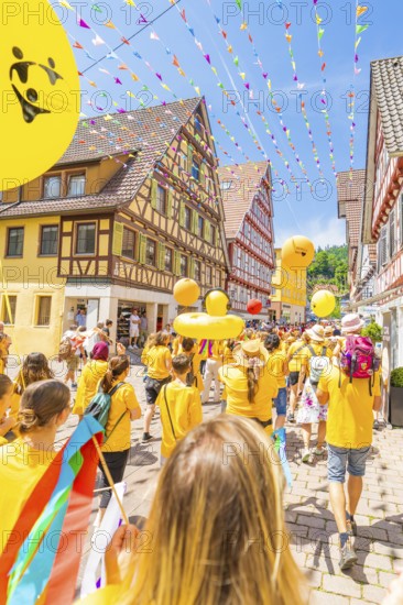 People in yellow clothes walk under colourful pennants in a narrow street in front of traditional houses, 950 years Calw, parade Calw, Black Forest, Germany