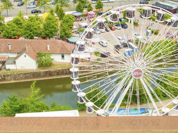 Ferris wheel stands next to a river and car parks, surrounded by trees in summer, 950 years of Calw, Calw parade, Black Forest, Germany