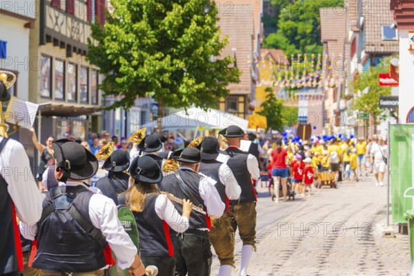 People in traditional costumes musically follow a parade on a sunny village street, 950 years Calw, parade Calw, Black Forest, Germany