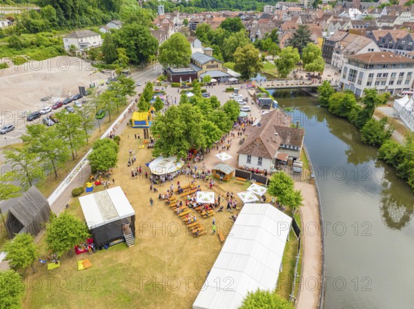 Aerial view of a town festival with people and tents on the riverbank next to historical architecture, 950 years of Calw, Calw parade, Black Forest, Germany