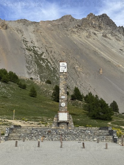 At Alpine pass Col de l'Izoard d'Izoard 2360 metres high road pass at pass summit of mountain road pass road 1934 erected altitude marker monument stele memorial column made of natural stone in memory of dedicated to General Baron Berge and workers of road construction, Cervières, Department Hautes-Alpes, Provence-Alpes-Cote d'Azur, France