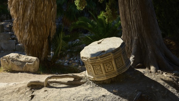An old, dilapidated stone cylinder lies in the sunshine next to a tree, Ancient Agora, Kos Town, Kos, Dodecanese, Greek Islands, Greece