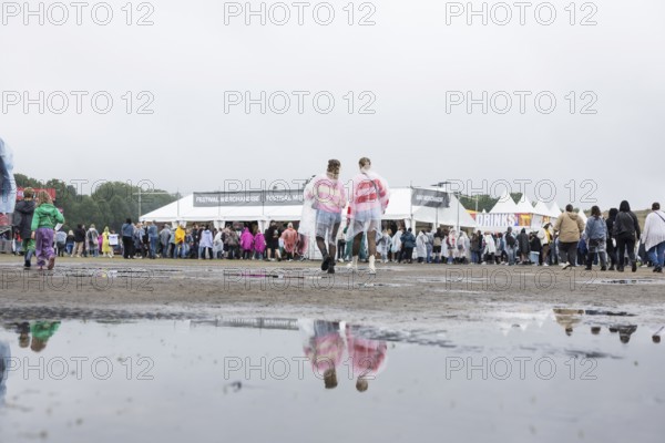 Festival-goers reflected in a puddle at the Lollapalooza Festival in the Olympic Stadium and on the Maifeld, Berlin, 12 July 2025