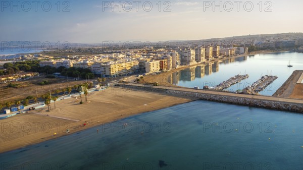 Aerial view of torrevieja coastline reflecting in mediterranean sea at sunrise, featuring acequion and naufragos coves, buildings, beaches, and harbor