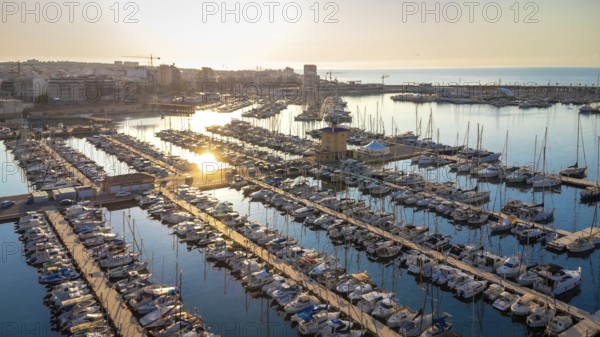 Golden sunrise reflecting on calm waters of torrevieja marina, showcasing docked boats and the cityscape in the background