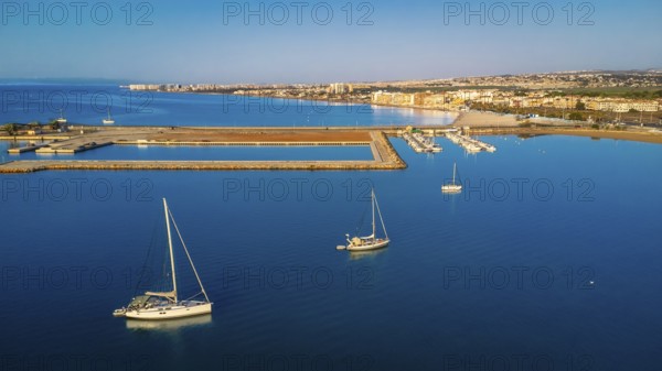 Stunning aerial view of sailboats floating on calm blue water near the coastline of torrevieja city, featuring a vibrant cityscape under a clear sky