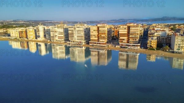Aerial view of torrevieja skyline reflecting on calm mediterranean sea at sunrise, with colorful buildings and tranquil waters creating a peaceful scene