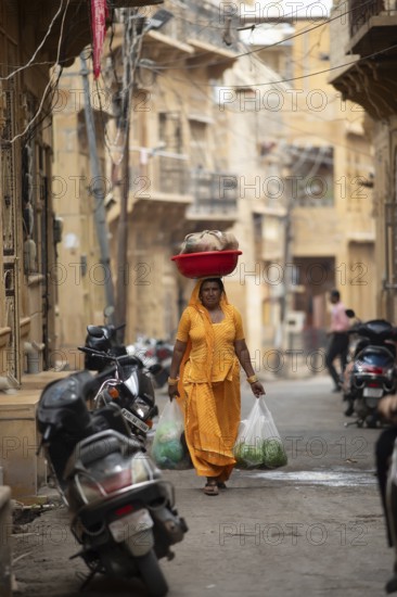 Indian woman carrying a bowl on her head in the old town of Jaisalmer, Rajasthan, India