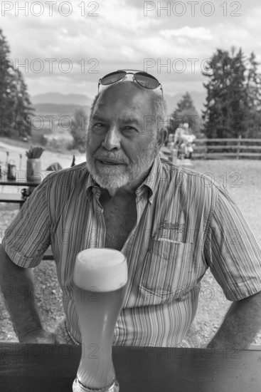 Elderly gentleman with beard and sunglasses in a garden restaurant with a drink, black and white, Bavaria, Germany