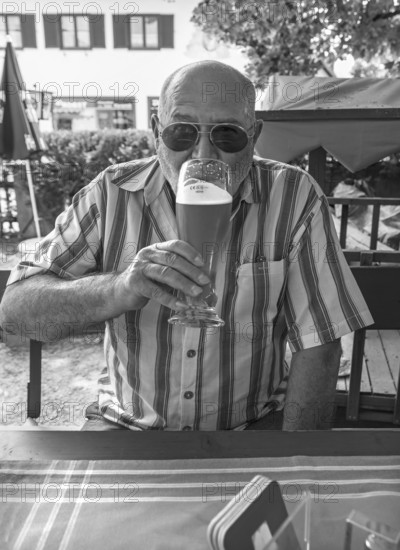 Senior with sunglasses drinking a wheat beer in a beer garden, black and white, Upper Bavaria, Germany