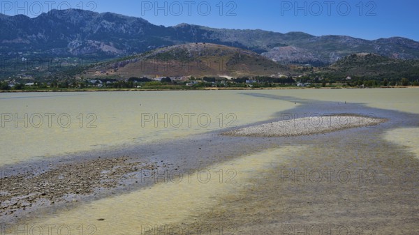 A lake with a long gravel bank and mountains in the background under a blue sky, salt lake, Tigaki, nature reserve, hydro biotope, Kos, Dodecanese, Greek Islands, Greece