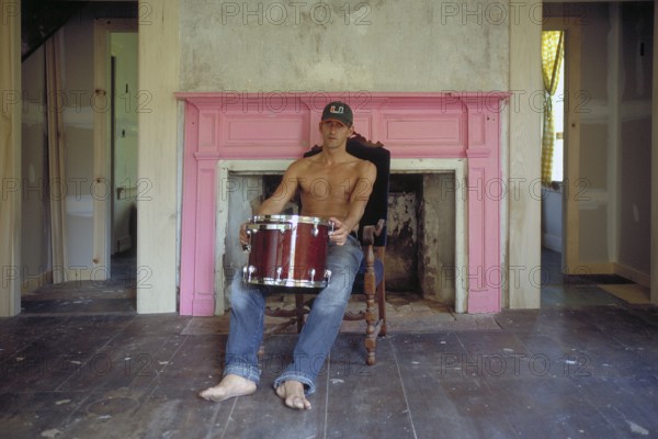 Young man with his drums in an empty room in front of a fireplace, New Jersey, USA
