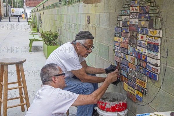 Detroit, Michigan - The city of Detroit is opening nine 'Arts Alleys' in neighborhoods around the city. Artist Vito J. Valdez (black cap) makes a ceramic mural on the Bagley Arts Alley with tiles handmade by residents of the Mexican-American community. He is assisted by Robert Ybarra