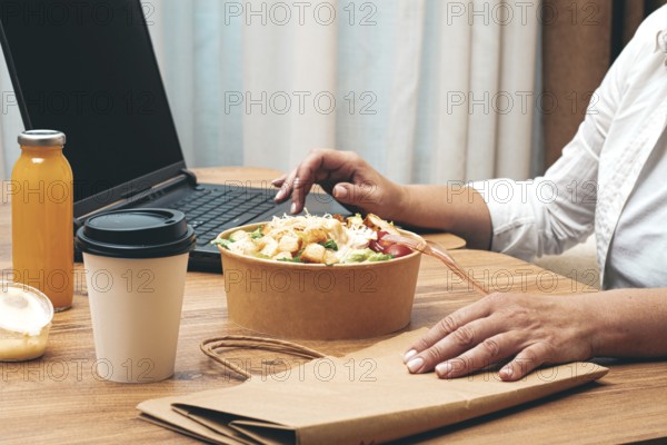 A woman is working on a laptop at home, there is food on the table, salad, coffee and juice, delivery, work at home