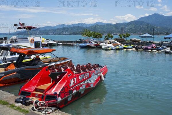 A red jet boat in the foreground of a harbor surrounded by other boats and mountains in the background, Batumi, Black Sea, Ajara region, Adjara, Autonomous Republic, Georgia