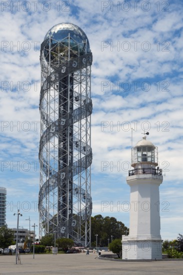 A tall spiral tower next to a white lighthouse under cloudy sky, Alphabetic Tower, Georgian Alphabet Tower, Miracle Park, Batumi Lighthouse, Black Sea, Adjara Region, Adjara, Autonomous Republic, Georgia