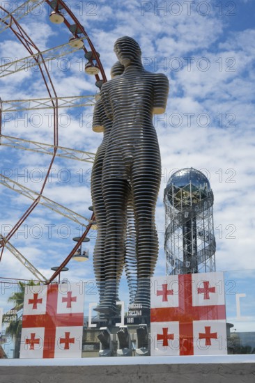 Metal sculptures of a man and a woman in front of a Ferris wheel with Georgian flags, the statue of Ali and Nino, Alphabetic Tower, Georgian Alphabet Tower, Miracle Park, Batumi, Black Sea, Adjara region, Adjara, autonomous republic, Georgia