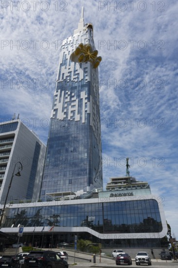 A large high-rise building with a glass façade stands in an urban environment. The sky is cloudy, cars are on the road, Batumi Tower with Ferris wheel, Batumi, Black Sea, Ajara region, Adjara, Autonomous Republic, Georgia