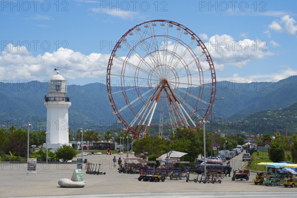 Big Ferris wheel and white lighthouse with mountains in the background under blue sky, amusement park, Batumi, Black Sea, Ajara region, Adjara, autonomous republic, Georgia