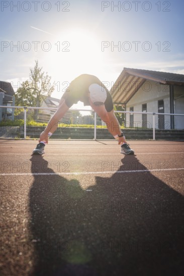 Runner stretching on a running track in strong sunlight early in the morning, Triathlon, Calw, Germany