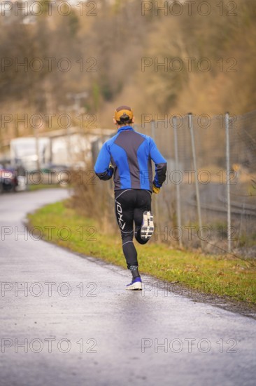 Man running on asphalt road wearing blue and black sportswear, triathlon, Calw, Germany