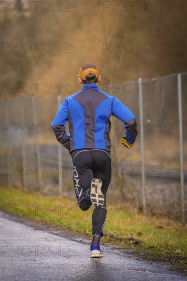 Back view of a runner on a country road wearing blue and black running clothes, triathlon, Calw, Germany