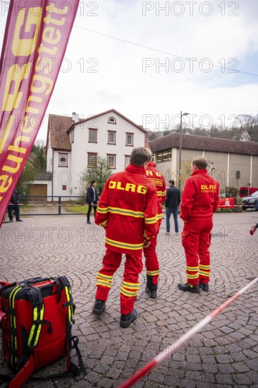 DLRG personnel wearing red uniforms stand on a paved square in front of buildings, Triathlon, Calw, Germany