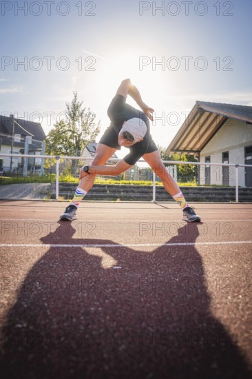 Man stretching on a running track in sunlight, triathlon, Calw, Germany
