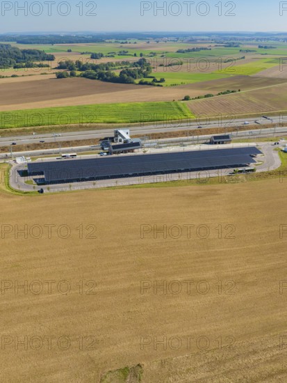 Solar system next to a motorway, surrounded by fields under clear skies, e-charging park, Merklingen, Germany