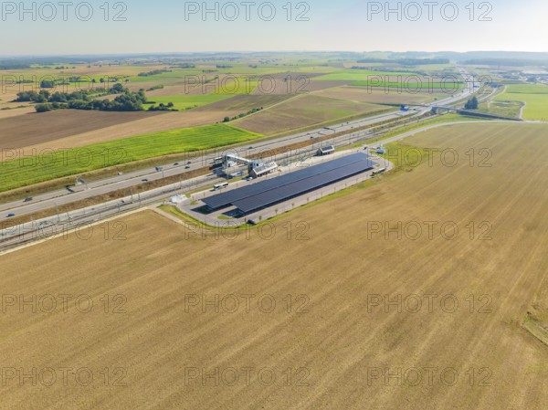 Solar system and motorway run parallel through wide fields under clear skies, e-charging park, Merklingen, Germany