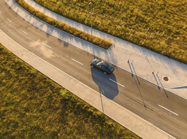 Aerial view of a car on a paved road next to a field in sunlight, BMW i7 electric car, Deer E-Carsharing, Calw, Germany