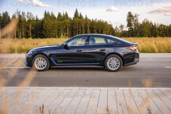 Black car on a road next to a field and forest under a blue sky, BMW i7 electric car, Deer E- Carsharing, Calw, Germany